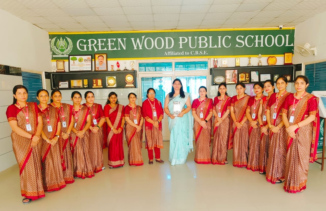Greenwood Public School Principal Mrs. Promila and teachers in traditional attire under CBSE affiliation banner with trophies